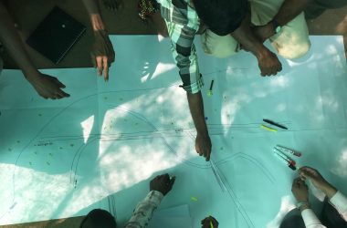 Group planning road design with drawings and tools outdoors.